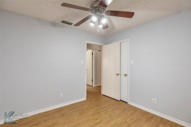 spare room featuring light wood-type flooring, baseboards, visible vents, and a textured ceiling