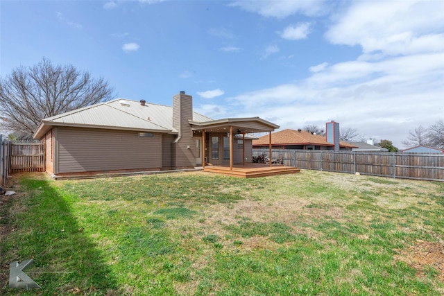 rear view of house with a lawn, a fenced backyard, a chimney, metal roof, and a wooden deck