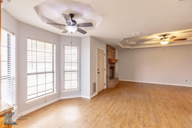 unfurnished living room with baseboards, a fireplace, a raised ceiling, and light wood-style floors