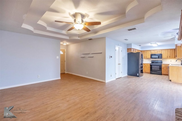 unfurnished living room featuring visible vents, a raised ceiling, ceiling fan, light wood-type flooring, and a sink