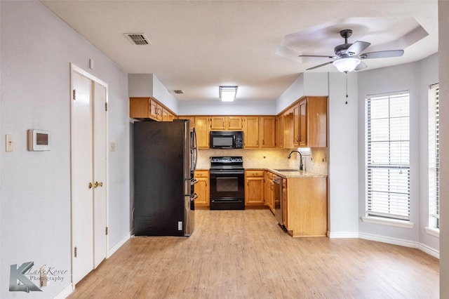 kitchen featuring a sink, light wood-type flooring, backsplash, black appliances, and plenty of natural light