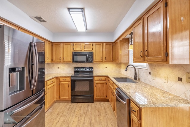 kitchen with tasteful backsplash, a sink, light stone countertops, light wood-type flooring, and black appliances