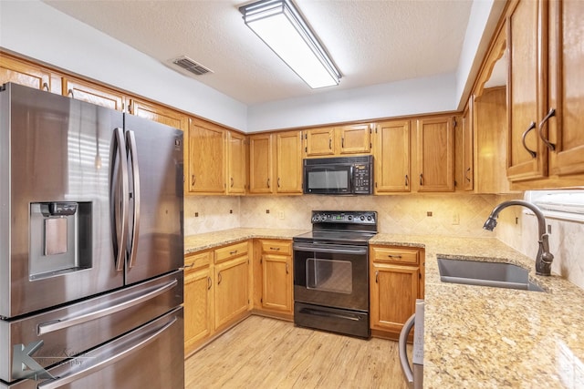 kitchen with visible vents, light wood-style flooring, light stone countertops, black appliances, and a sink