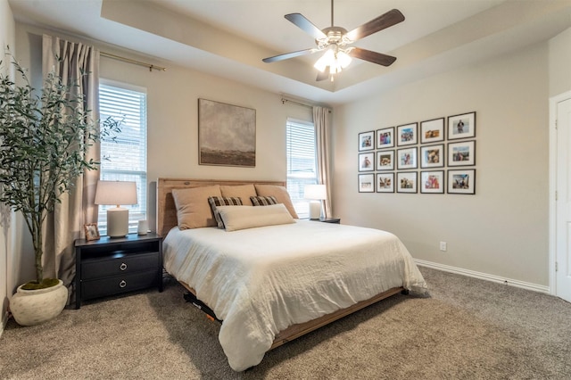 carpeted bedroom with baseboards, a tray ceiling, and a ceiling fan