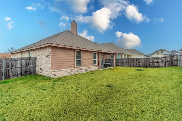 back of property featuring a fenced backyard, a chimney, a lawn, and brick siding