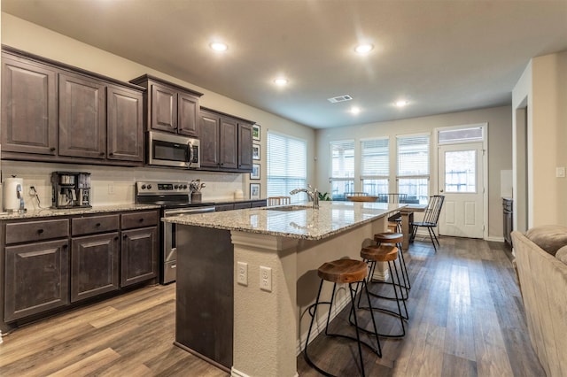 kitchen with dark brown cabinetry, a breakfast bar, wood finished floors, visible vents, and appliances with stainless steel finishes