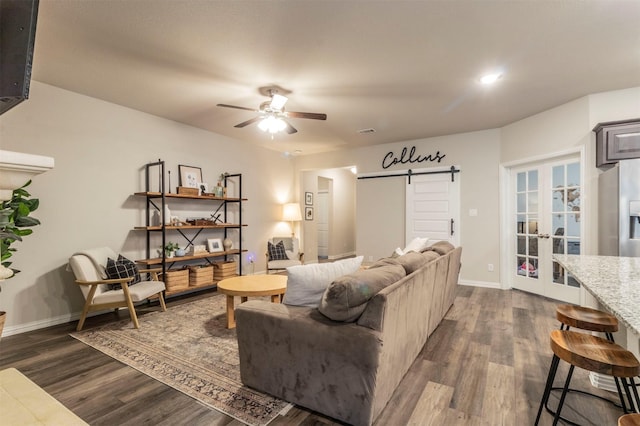 living room featuring a barn door, dark wood-style flooring, a ceiling fan, baseboards, and french doors