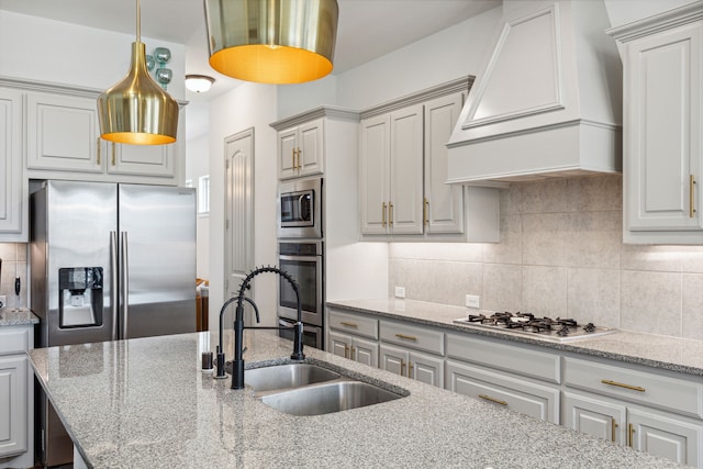 kitchen with custom exhaust hood, hanging light fixtures, decorative backsplash, appliances with stainless steel finishes, and a sink