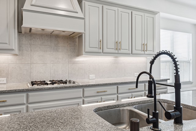 kitchen featuring light stone counters, stainless steel gas cooktop, backsplash, a sink, and premium range hood