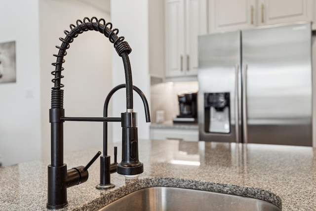 details with stone countertops, stainless steel fridge, and white cabinetry