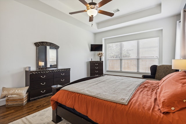 bedroom featuring a raised ceiling, visible vents, dark wood finished floors, and ceiling fan