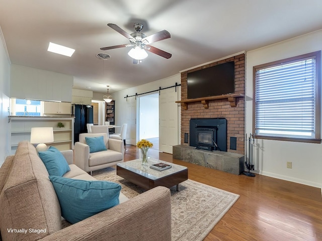 living area featuring visible vents, a barn door, a ceiling fan, wood finished floors, and baseboards