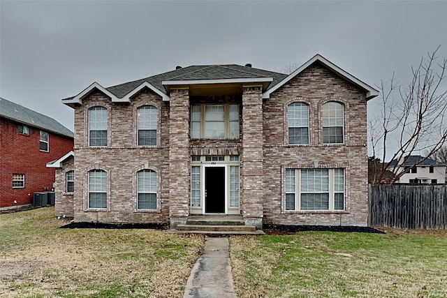 traditional-style home featuring central air condition unit, brick siding, a shingled roof, fence, and a front yard