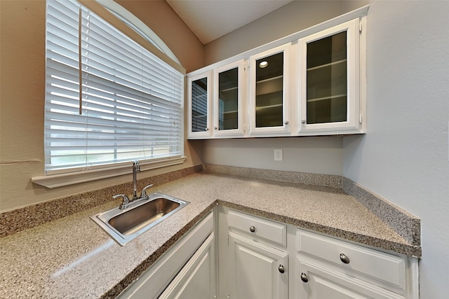 kitchen featuring glass insert cabinets, light countertops, white cabinets, and a sink