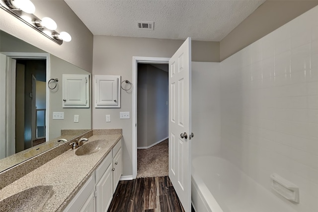 full bath featuring a textured ceiling, wood finished floors, vanity, visible vents, and baseboards