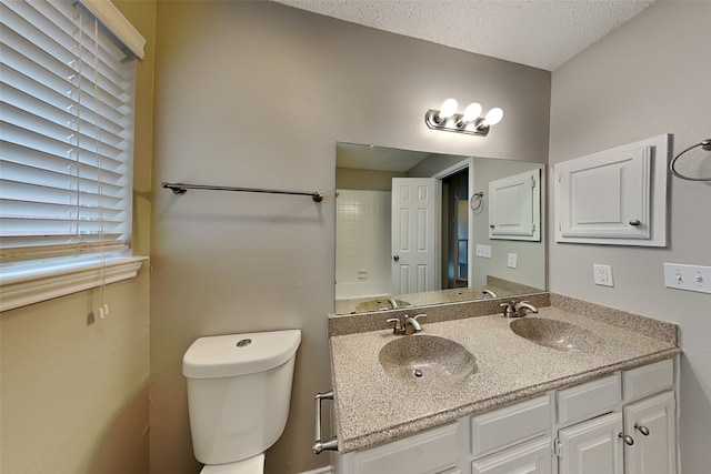 bathroom with a textured ceiling, double vanity, a sink, and toilet