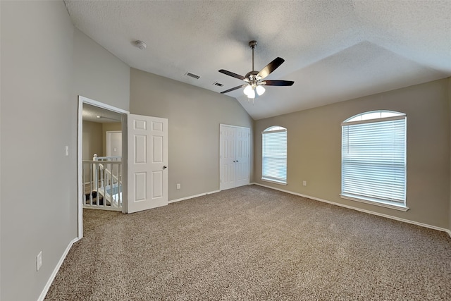 spare room with carpet, lofted ceiling, visible vents, a ceiling fan, and a textured ceiling