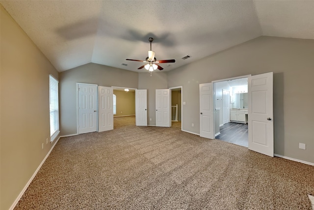 unfurnished bedroom with lofted ceiling, carpet flooring, visible vents, baseboards, and ensuite bath