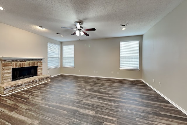 unfurnished living room featuring dark wood-style floors, plenty of natural light, a fireplace, and visible vents