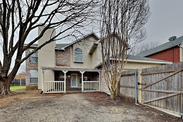 view of front facade with a porch, a gate, brick siding, and fence