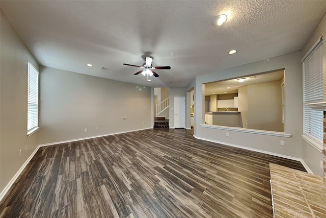 unfurnished living room featuring a wealth of natural light, stairway, a textured ceiling, wood finished floors, and baseboards