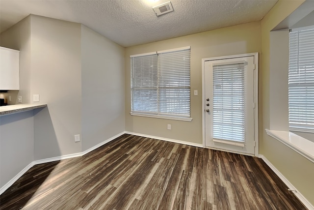 unfurnished dining area featuring a textured ceiling, wood finished floors, visible vents, and baseboards