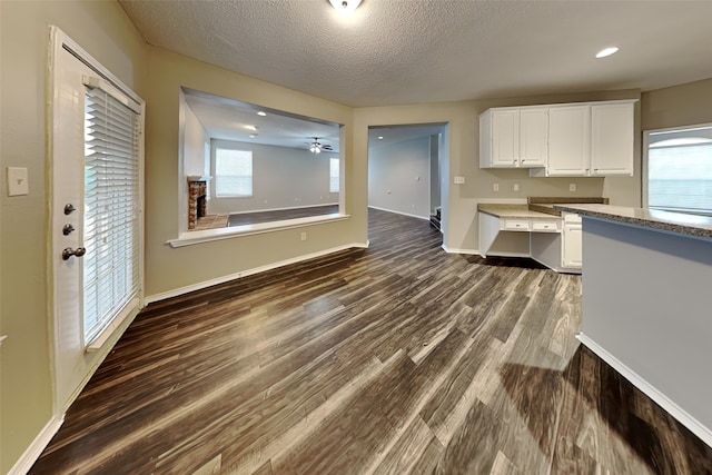 kitchen featuring a textured ceiling, dark wood-type flooring, white cabinetry, a healthy amount of sunlight, and baseboards