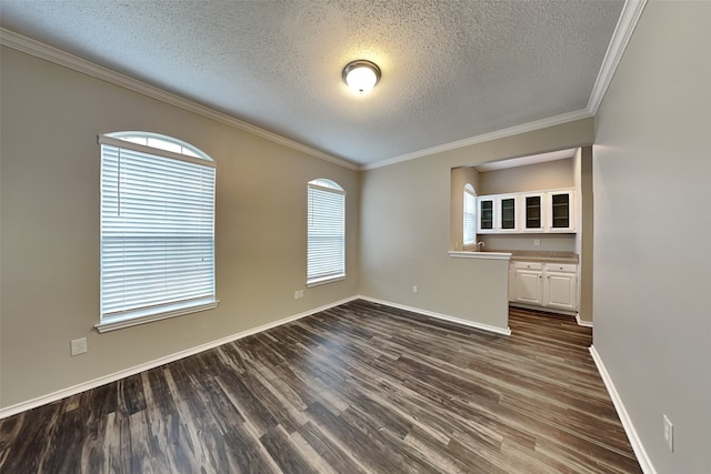 empty room featuring dark wood-style floors, a textured ceiling, baseboards, and crown molding