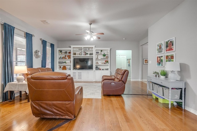 living room with light wood-style flooring, visible vents, ceiling fan, and baseboards