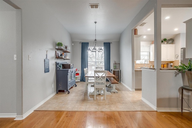 dining space with light wood finished floors, baseboards, visible vents, and a chandelier