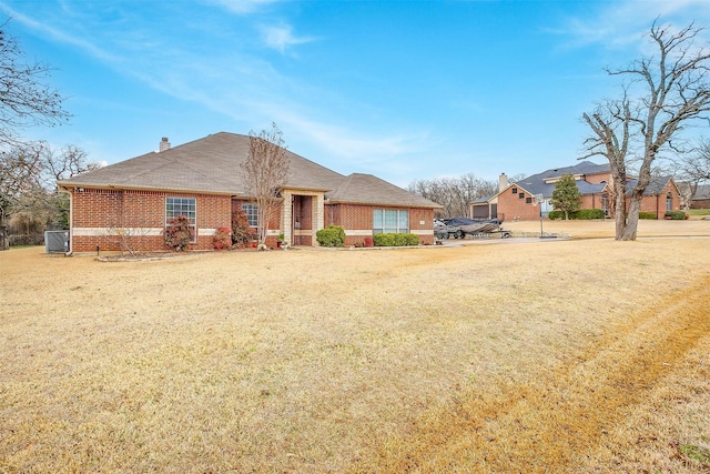 view of front of home with a front yard, a chimney, cooling unit, and brick siding