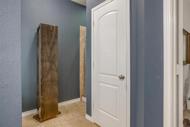 bathroom with baseboards, a shower, a textured wall, and tile patterned floors