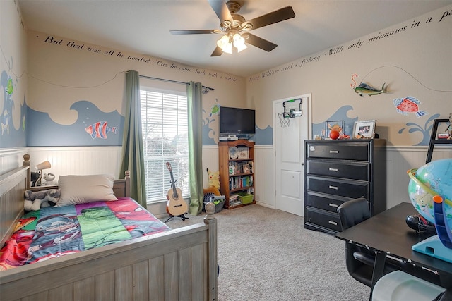 carpeted bedroom featuring a wainscoted wall and a ceiling fan