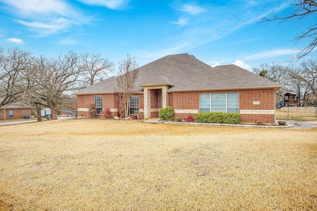 view of front facade featuring a shingled roof, brick siding, fence, and a front lawn