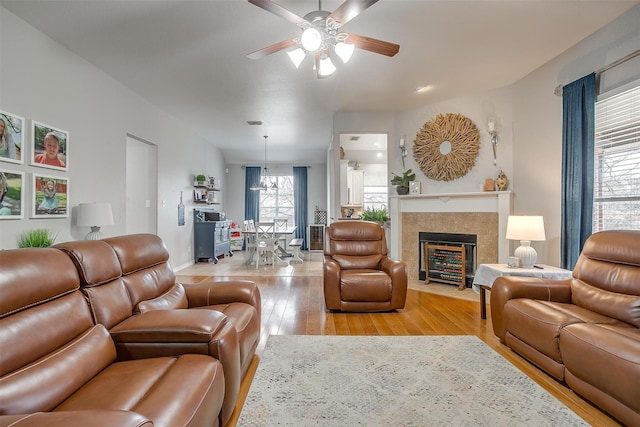 living area with light wood-type flooring, a fireplace with flush hearth, baseboards, and ceiling fan with notable chandelier