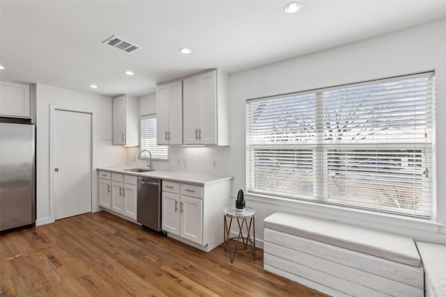 kitchen with stainless steel appliances, light countertops, visible vents, a sink, and wood finished floors