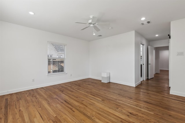 spare room with a barn door, visible vents, ceiling fan, and wood finished floors