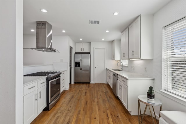 kitchen featuring stainless steel appliances, visible vents, white cabinets, light countertops, and wall chimney range hood