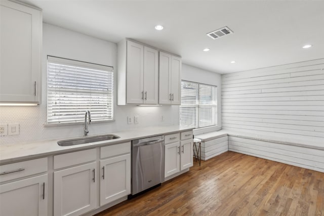 kitchen with visible vents, stainless steel dishwasher, white cabinets, a sink, and wood finished floors