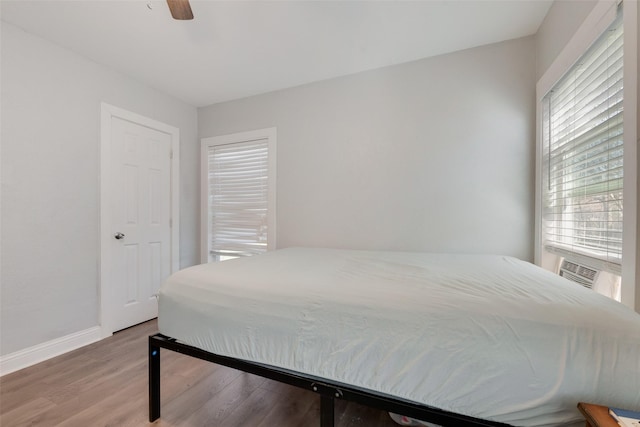 bedroom featuring a ceiling fan, cooling unit, baseboards, and wood finished floors