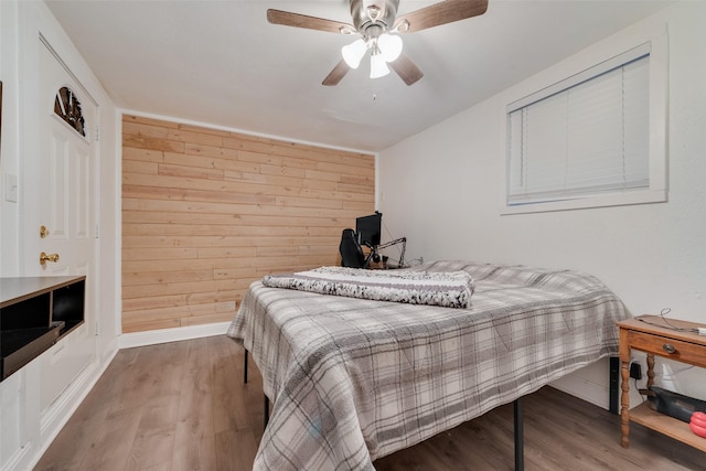 bedroom featuring a ceiling fan, wood walls, and wood finished floors