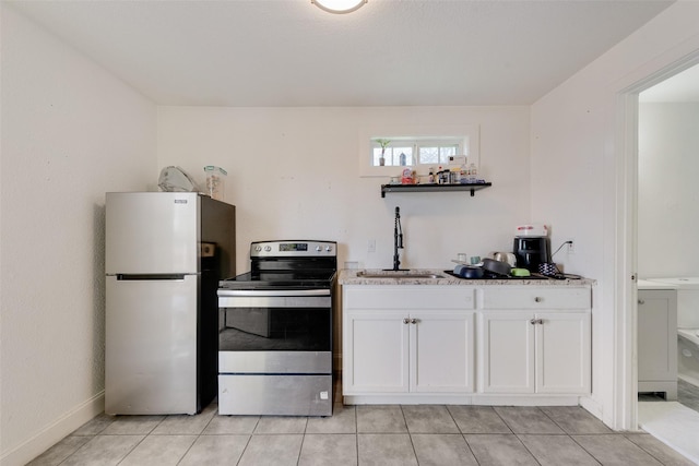 kitchen with light tile patterned floors, freestanding refrigerator, white cabinets, stainless steel range with electric cooktop, and a sink