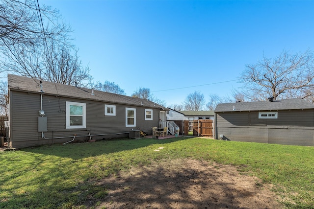 rear view of house with central AC unit, fence, and a lawn