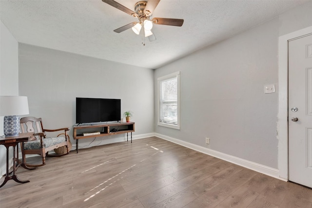 living room with a textured ceiling, baseboards, a ceiling fan, and light wood-style floors