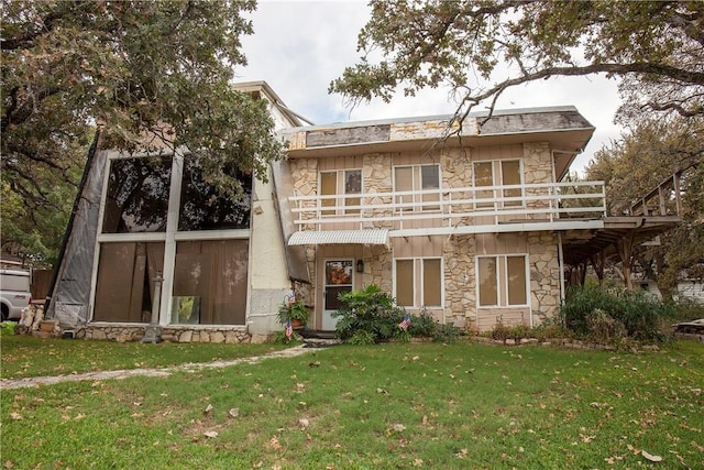 rear view of house featuring stone siding, a lawn, and a balcony