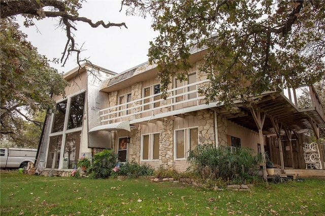 rear view of house with stone siding, a yard, and a balcony