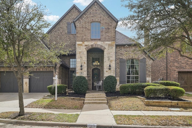 french country home featuring brick siding, stone siding, driveway, and a shingled roof