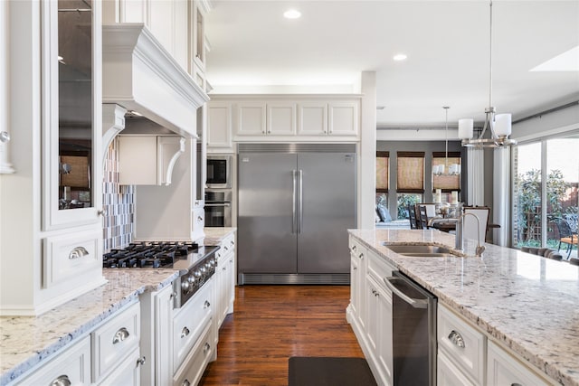 kitchen with dark wood-style floors, glass insert cabinets, built in appliances, an inviting chandelier, and white cabinetry