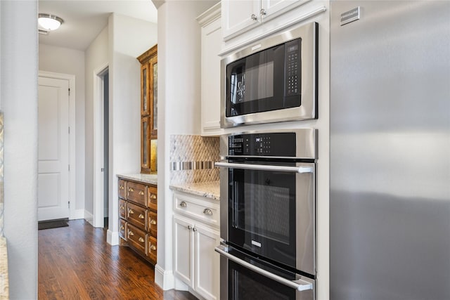 kitchen featuring light stone countertops, white cabinets, appliances with stainless steel finishes, decorative backsplash, and dark wood finished floors