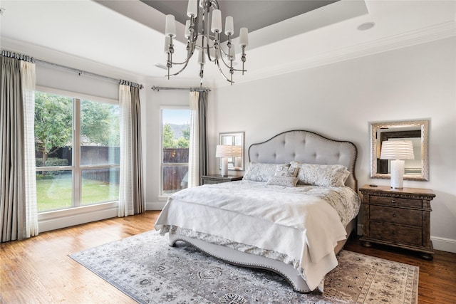 bedroom featuring baseboards, a raised ceiling, wood finished floors, crown molding, and a notable chandelier